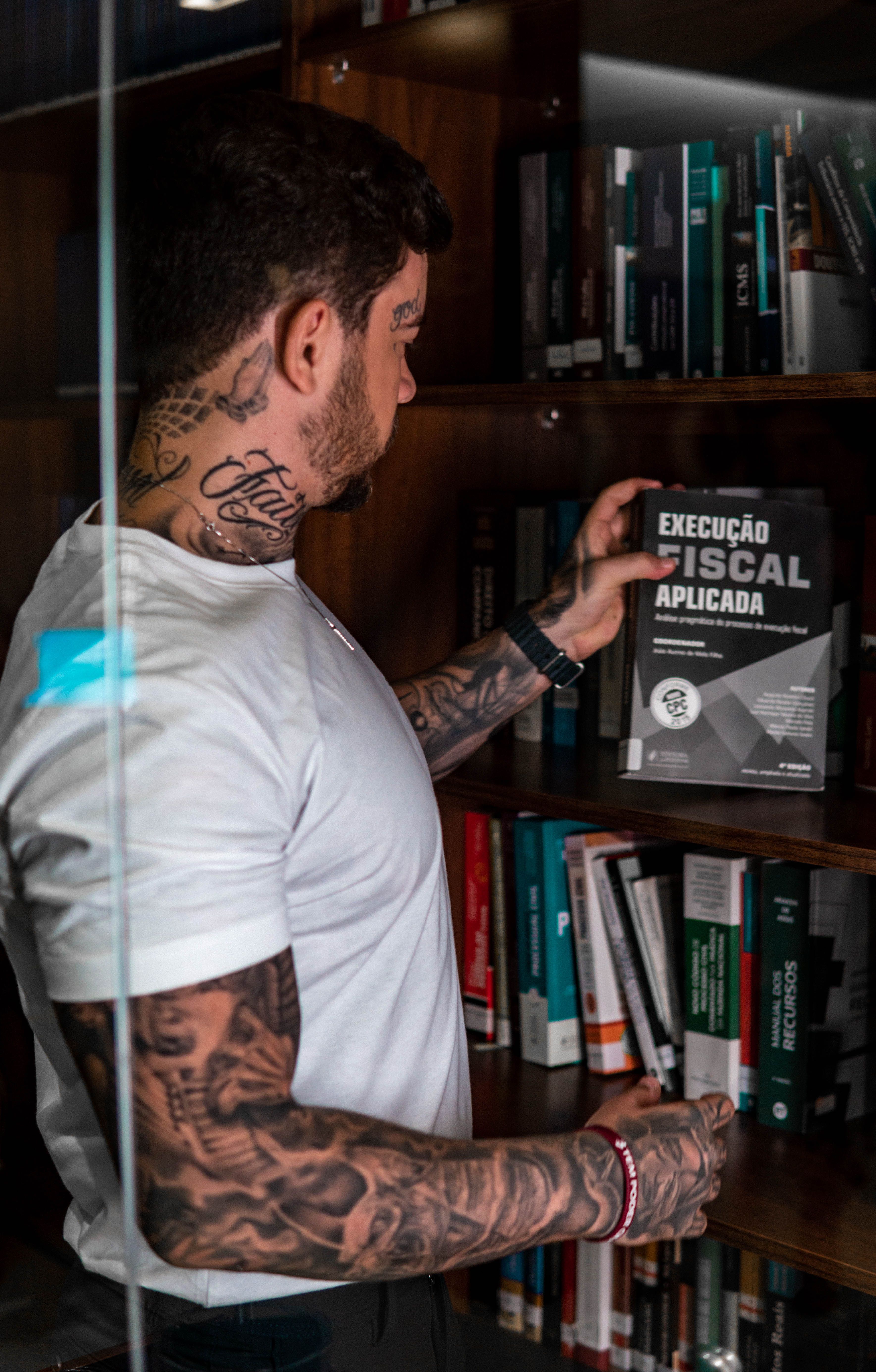 Homem com tatuagem no pescoço em ambiente do setor jurídico com prateleiras de livros